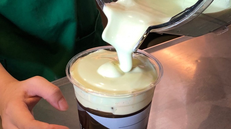 Close-up of a barista pouring cold foam on an iced coffee