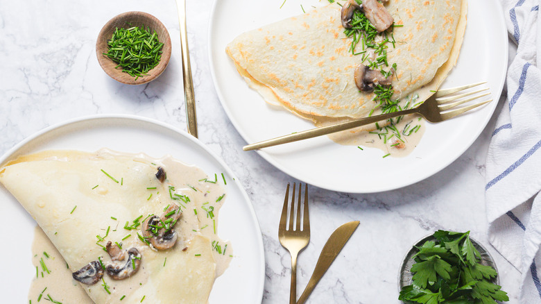 Two large crepes with mushrooms, cream sauce, chives and cutlery