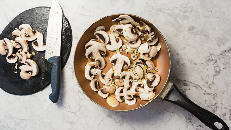 Pan with mushrooms and garlic besides board with knife and mushrooms