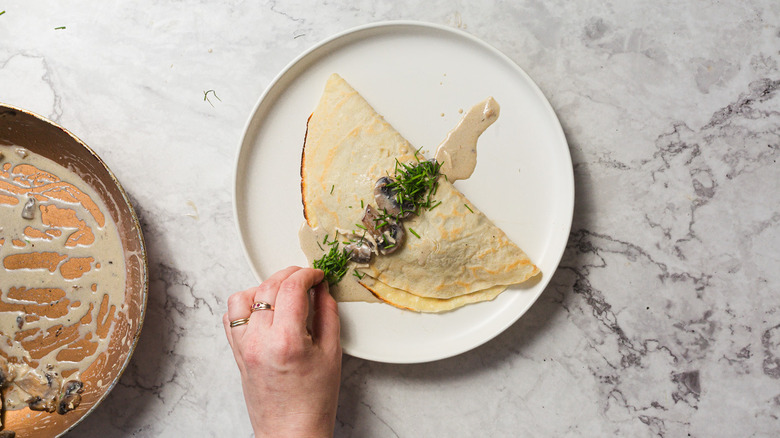 Hand putting chives on crepes