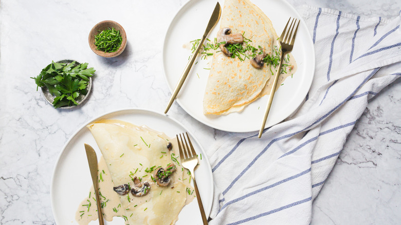 Two large crepes with mushrooms, cream sauce, chives and cutlery