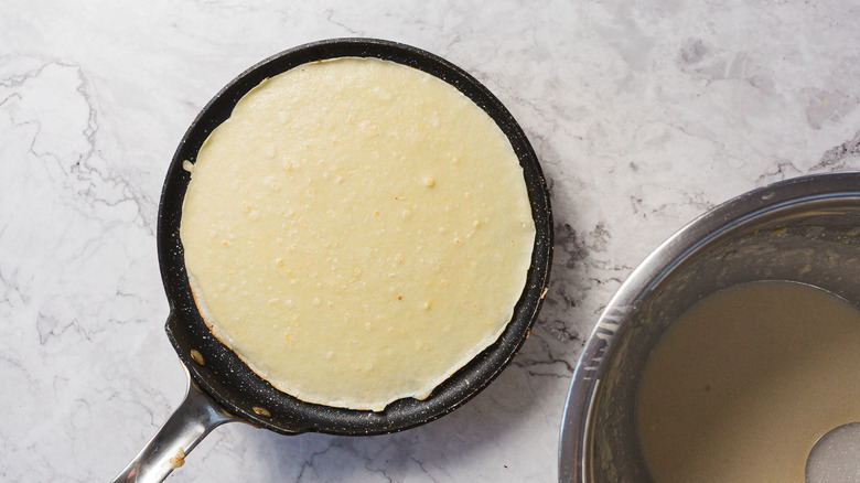 Crepe in pan besides batter in bowl