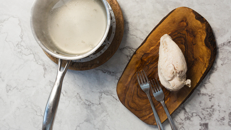 Cooked chicken on cutting board besides pan with water