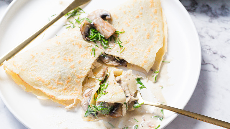 Crepe with mushrooms, cream sauce, chives and a cut taken out of it