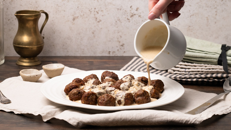 pouring cream sauce on meatballs