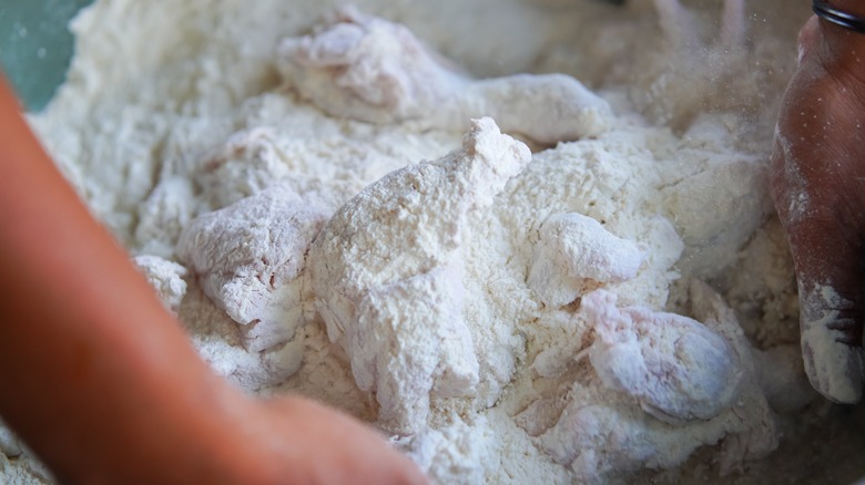 Hands mixing chicken pieces with flour for frying 