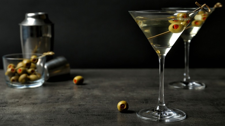 Two Martinis with a shaker and olives behind them