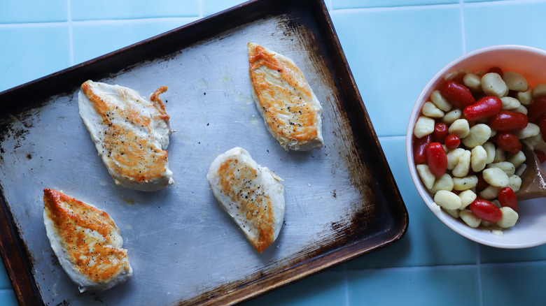 Oven roasted chicken breasts on tray next to gnocchi bowl