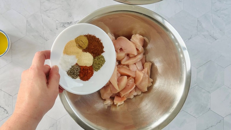 hand pouring spices on chicken