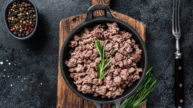 Ground beef in a cast iron skillet with peppercorns and fresh herbs