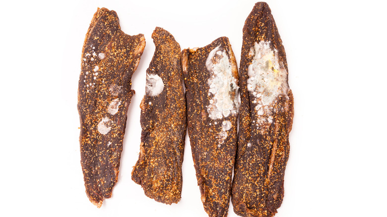 Four slices of moldy beef jerky on a white background