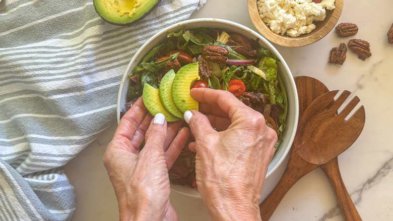 hand placing avocado on salad