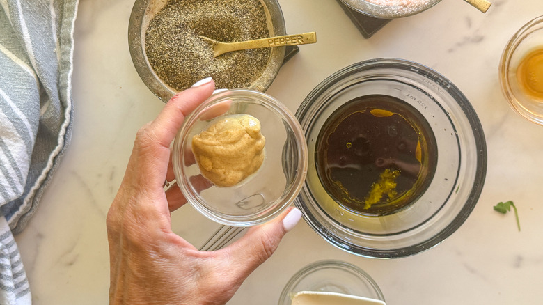 hand adding mustard to dressing