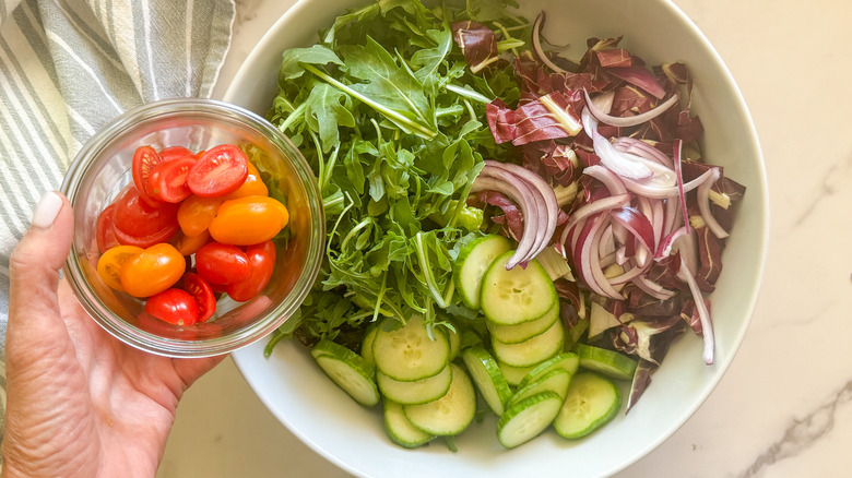 hand adding tomatoes to salad