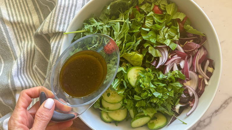 hand adding dressing to salad