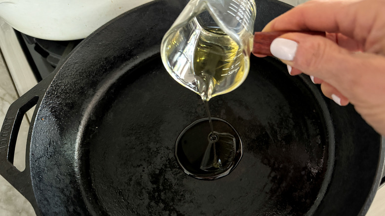 hand adding oil to skillet