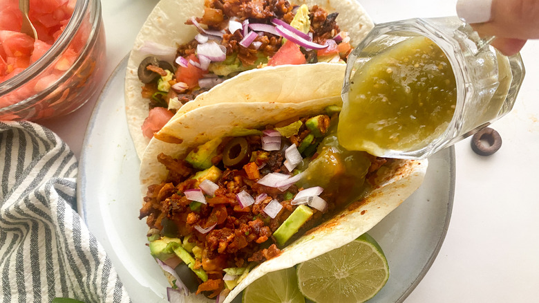 pouring green salsa on taco