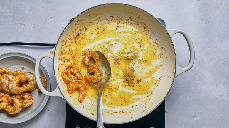 removing shrimp from skillet with metal spoon