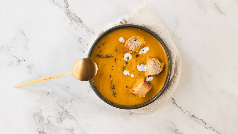 Overhead bowl of carrot soup with napkin and spoon