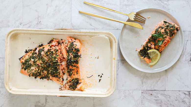 Salmon in plate with cutlery besides baking sheet