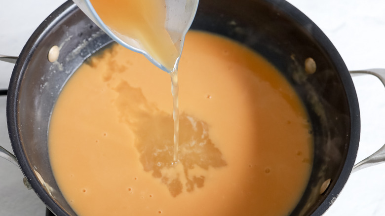 pouring chicken stock into saucepan