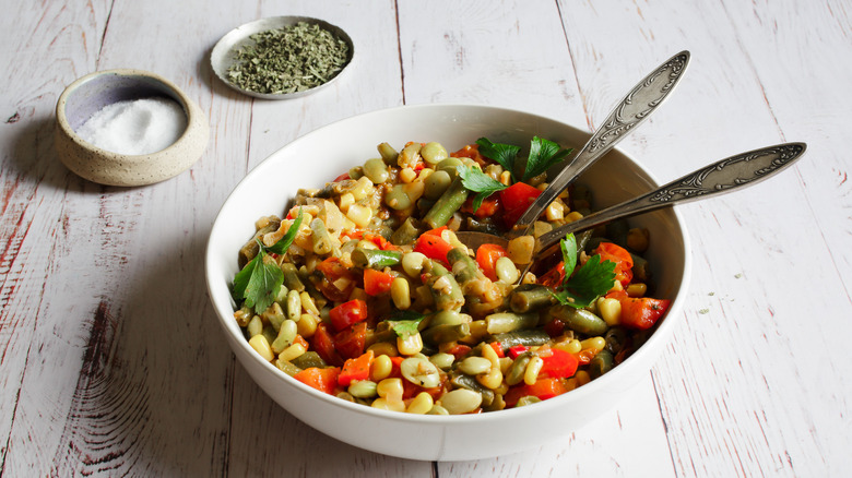 Bowl of succotash with spoons, salt and sage