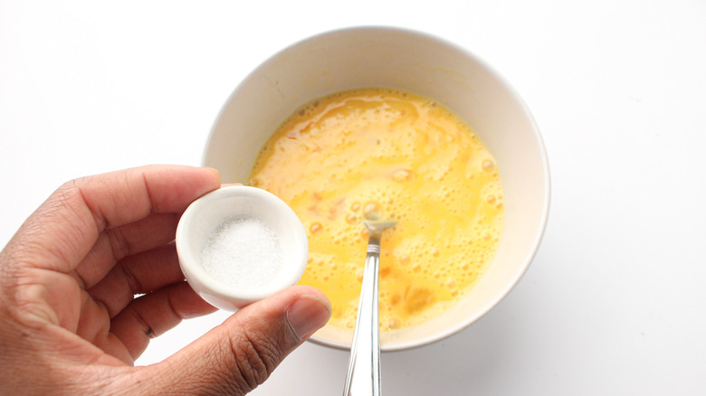 Hand adding salt to eggs