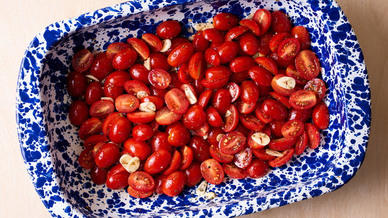 Grape tomatoes in a roasting pan with garlic.