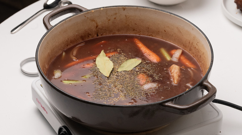 Broth, vegetables, and bay leaves in pan