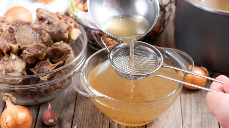 Straining bone broth into glass bowl