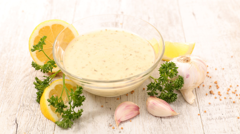 A bowl of lemon sauce surrounded by garlic, parsley, and lemons