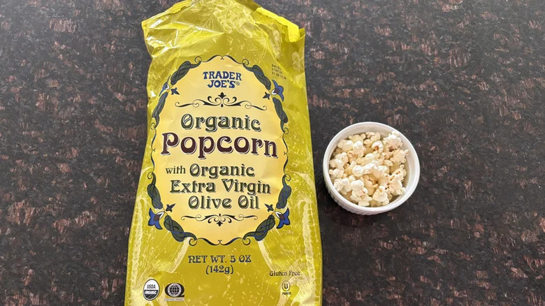 A bag of Trader Joe's Organic Popcorn with organic extra-virgin olive oil on a countertop next to a ramekin of popcorn