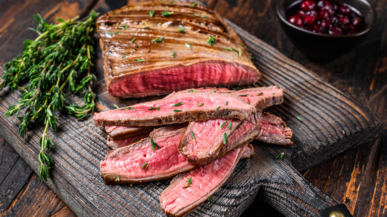 flank steak sliced on a board with herbs