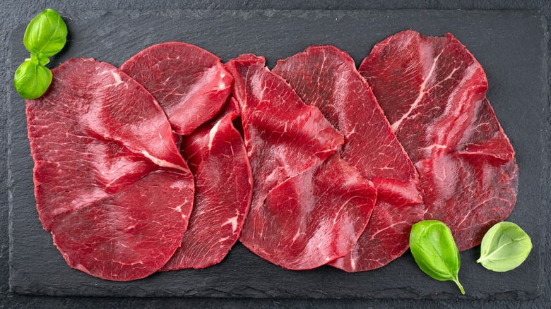 Beef carpaccio slices on slate with basil leaves