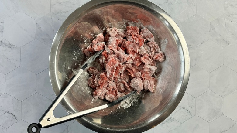 tongs stirring flour into beef