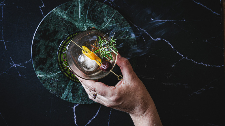 Hand holding cocktail with smoking rosemary branch