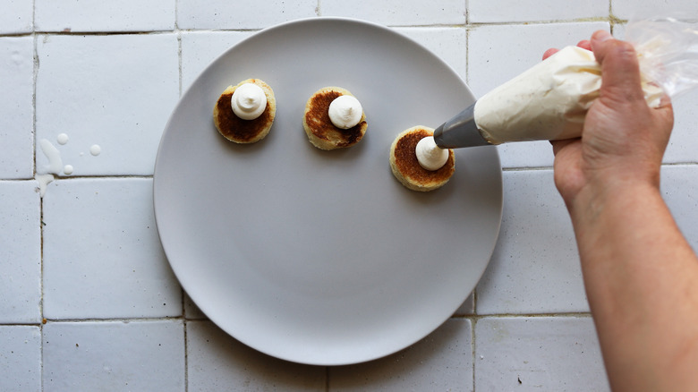 hand piping cream onto round bread bites