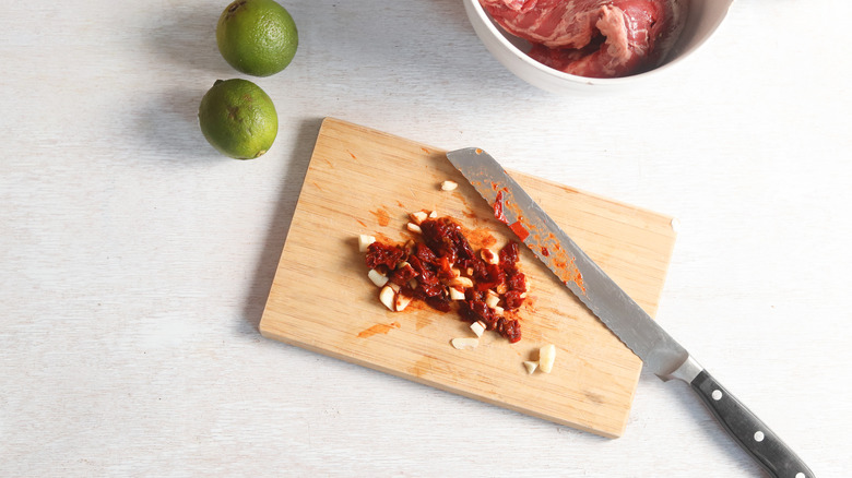 minced peppers and garlic on cutting board with knife