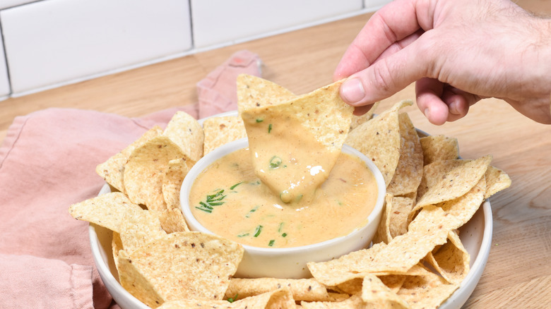 hand scooping tortilla chip into queso dip