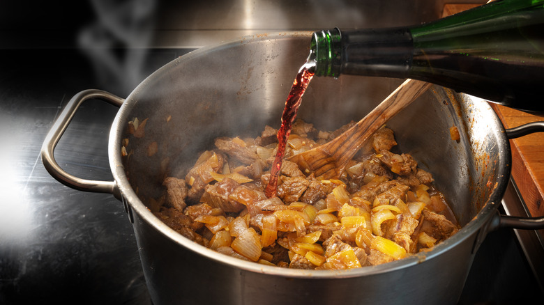 Red wine being poured into a pot of stew