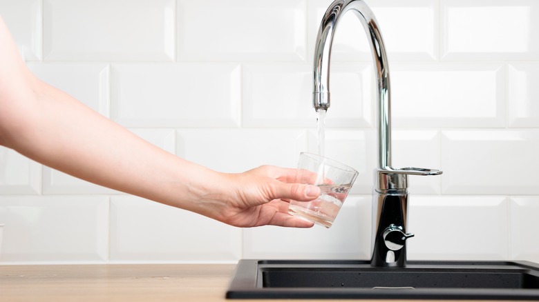 Hand filling a glass under a running faucet