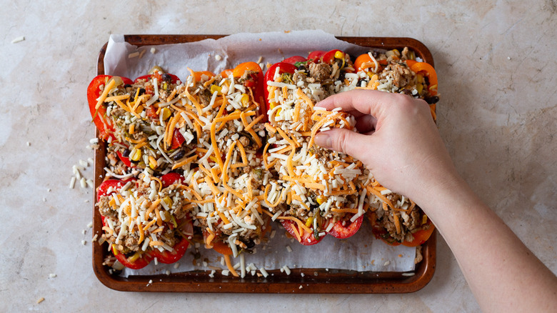 Topping stuffed peppers on baking sheet with cheese