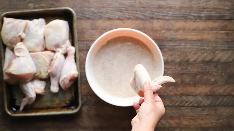 hand holding chicken over marinade