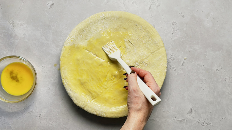 hand brushing egg wash onto pie