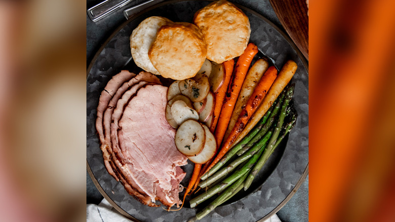 A spiral ham on a plate with vegetables and biscuits