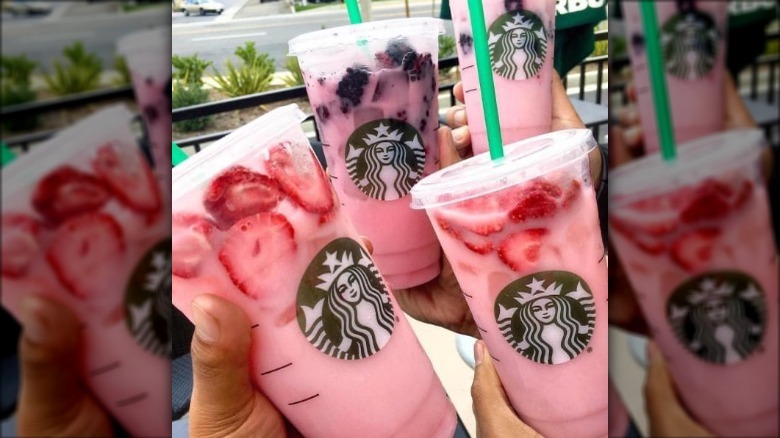 a group of people holding up starbucks pink drinks