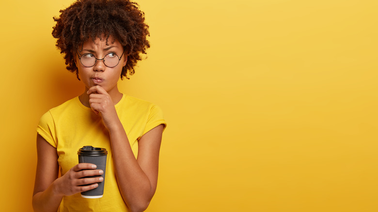 Woman holding coffee looking doubtful