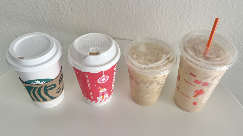 Four chai lattes from Starbucks and Dunkin' are lined up on a white table.