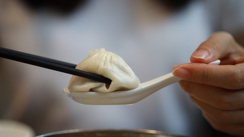 person placing a soup dumpling on a spoon