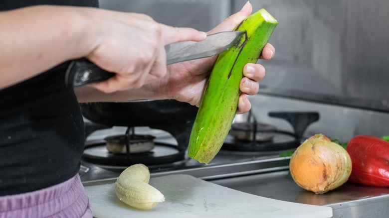 Hands cutting a green plantain with knife